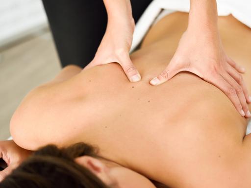 Zwei Hände massieren den Rücken einer Frau, die auf dem Bauch einer Massageliege liegt. Zwei Hände massieren den Rücken einer Frau, die auf dem Bauch einer Massageliege liegt.