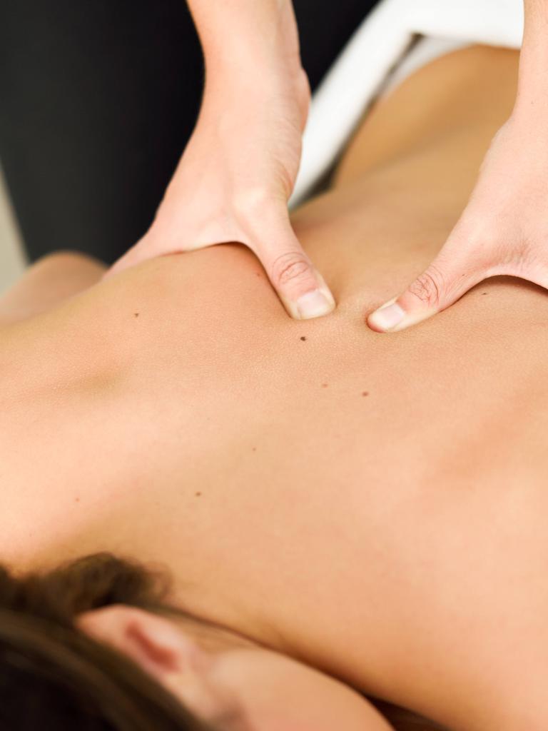 Zwei Hände massieren den Rücken einer Frau, die auf dem Bauch einer Massageliege liegt. Zwei Hände massieren den Rücken einer Frau, die auf dem Bauch einer Massageliege liegt.