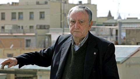Rafael Chirbes steht auf einem Balkon mit Blick über Barcelona und blickt ernst in die Kamera.