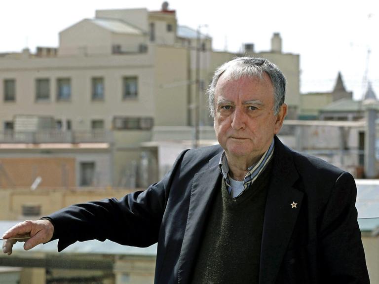Rafael Chirbes steht auf einem Balkon mit Blick über Barcelona und blickt ernst in die Kamera.