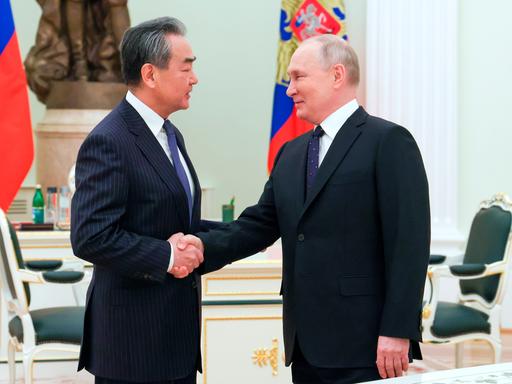 Der russische Präsident Wladimir Putin und Chinas oberster Außenpolitiker Wang Yi schütteln sich die Hände. Sie befinden sich im Kreml.