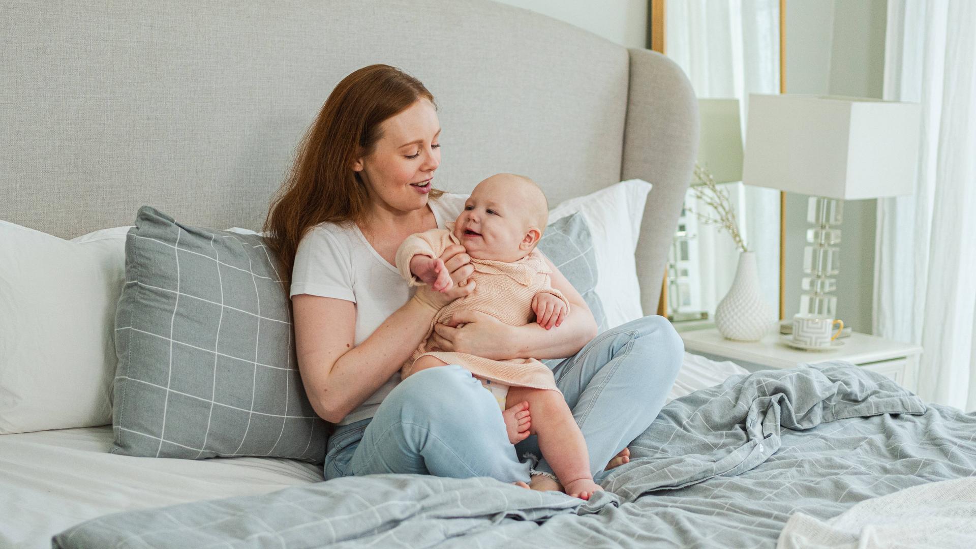 Glückliche Familie zu Hause. Mutter spielt mit Kleinkind auf dem Bett.