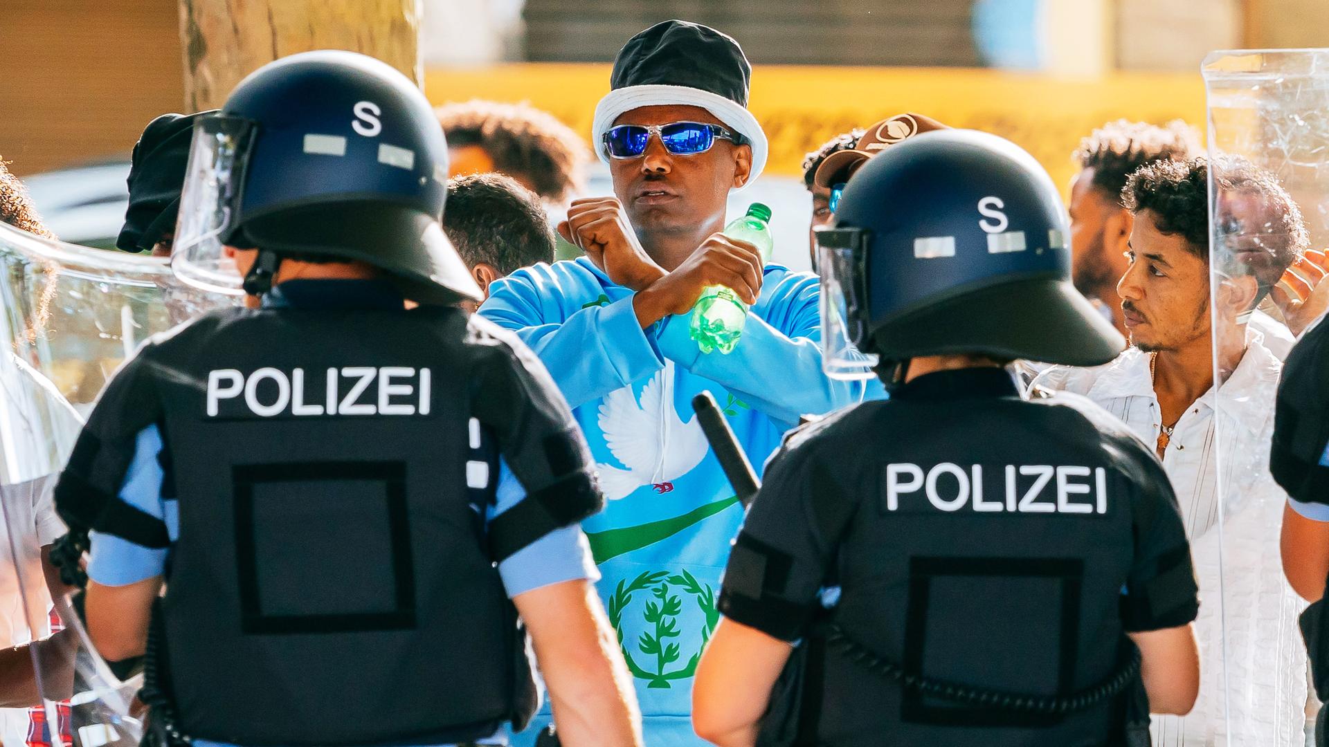 Ein Polizist und eine Polizistin mit Helmen stehen vor einer Gruppe Demonstranten. Ein Polizist und eine Polizistin mit Helmen stehen vor einer Gruppe Demonstranten.