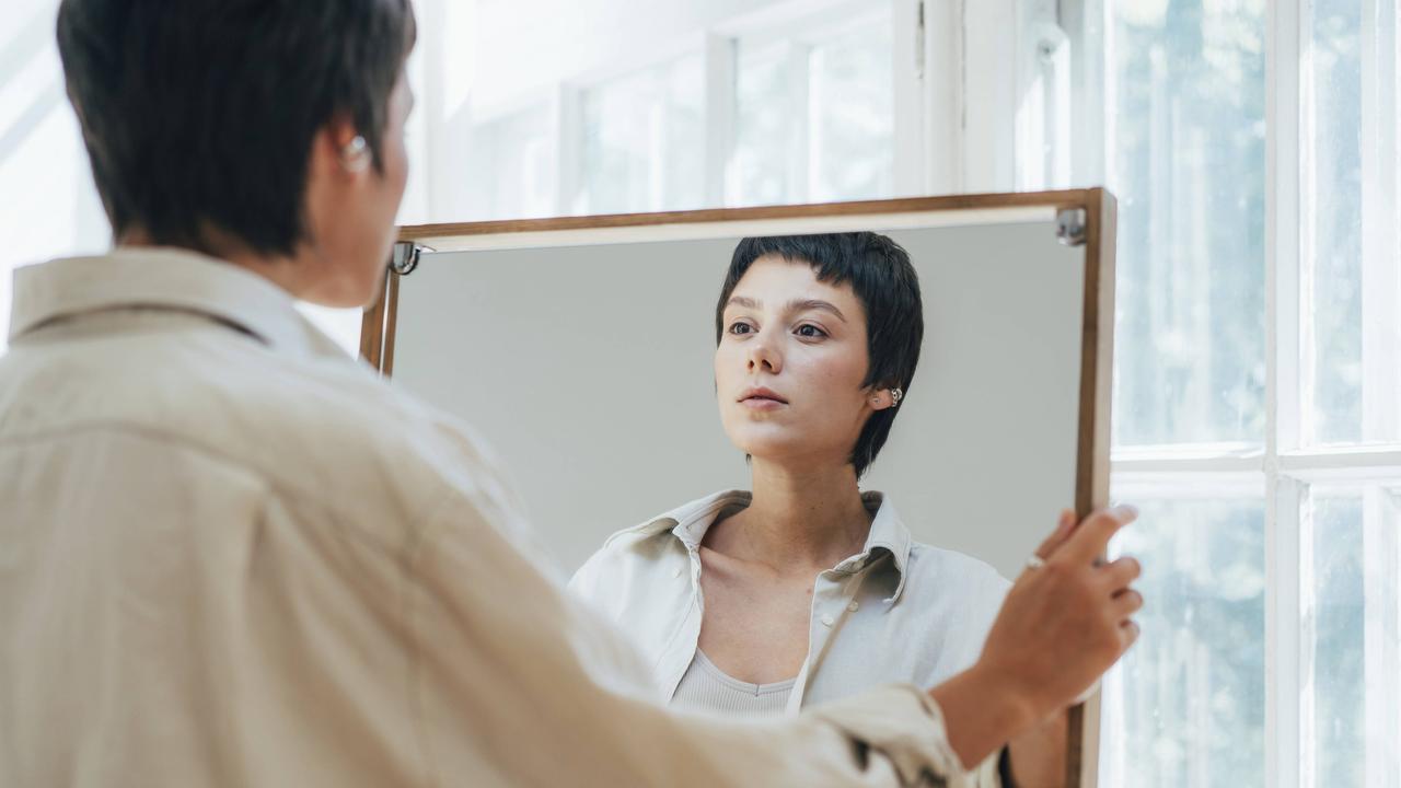 Eine junge Frau mit kurzen braunen Haaren betrachtet ihr Spiegelbild.