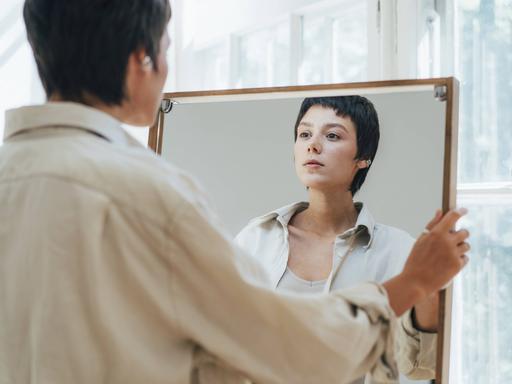 Eine junge Frau mit kurzen braunen Haaren betrachtet ihr Spiegelbild.