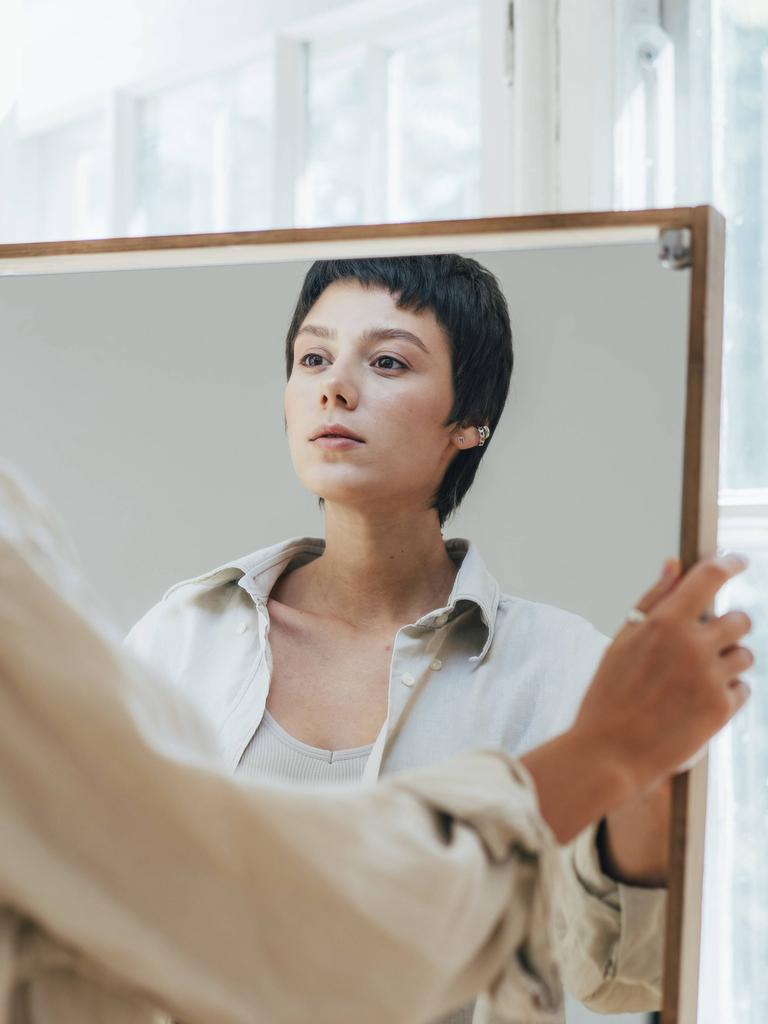 Eine junge Frau mit kurzen braunen Haaren betrachtet ihr Spiegelbild.
