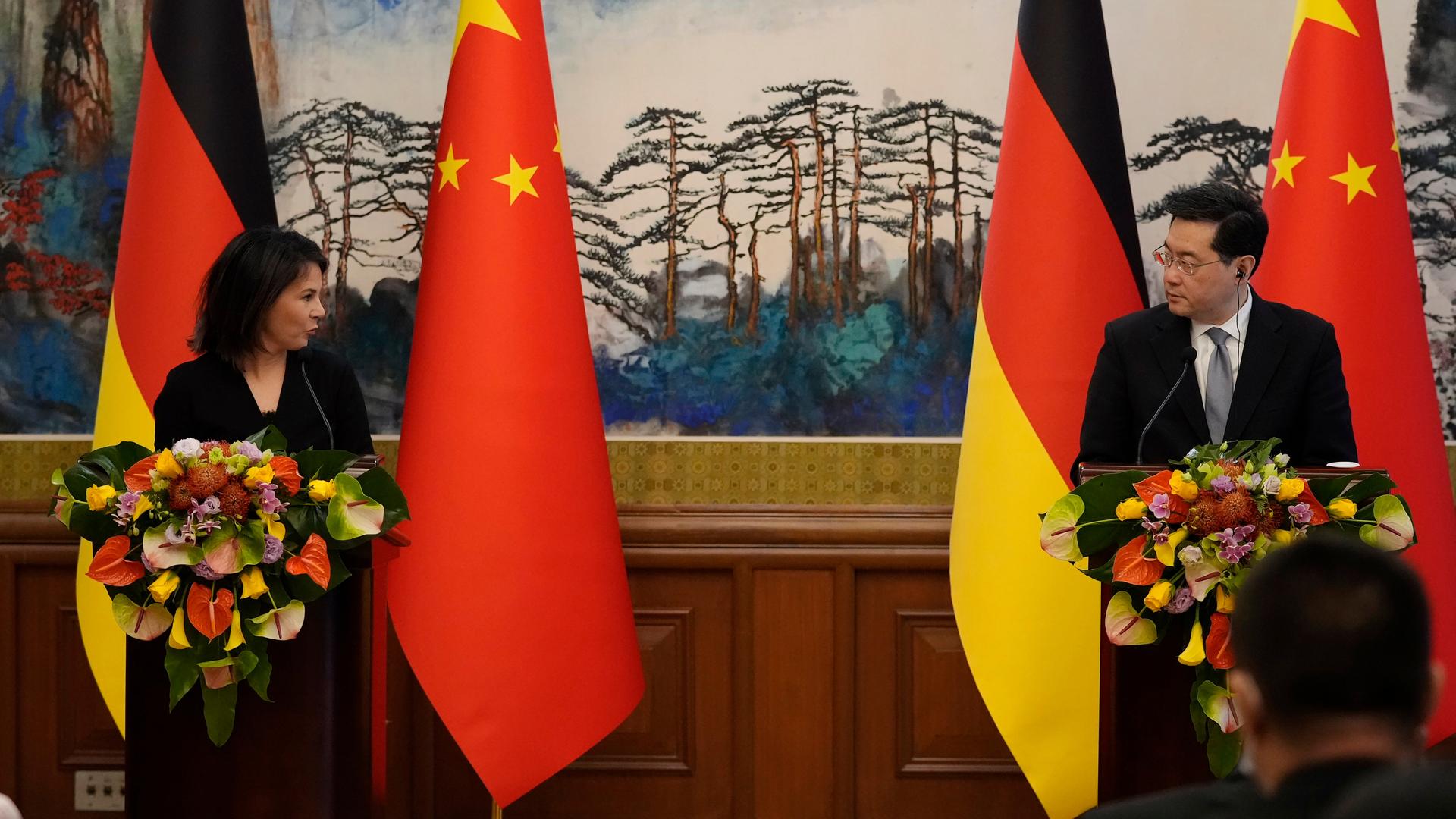 Bundesaußenministerin Baerbock und ihr chinesischer Kollege Qin Gang stehen hinter Rednerpulten, vor denen große Blumensträuße stehen und geben eine Pressekonferenz. Hinter ihnen jeweils die deutsche und die chinesische Flagge.