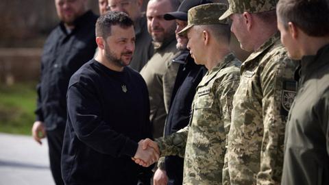 Der ukrainische Präsident Selenskyj schüttelt die Hand des Oberbefehlshabers der ukrainischen Streitkräfte Oleksandr Syrskyi (3R) an einer Gedenkstätte für die Opfer der russischen Besatzung in der Stadt Bucha.