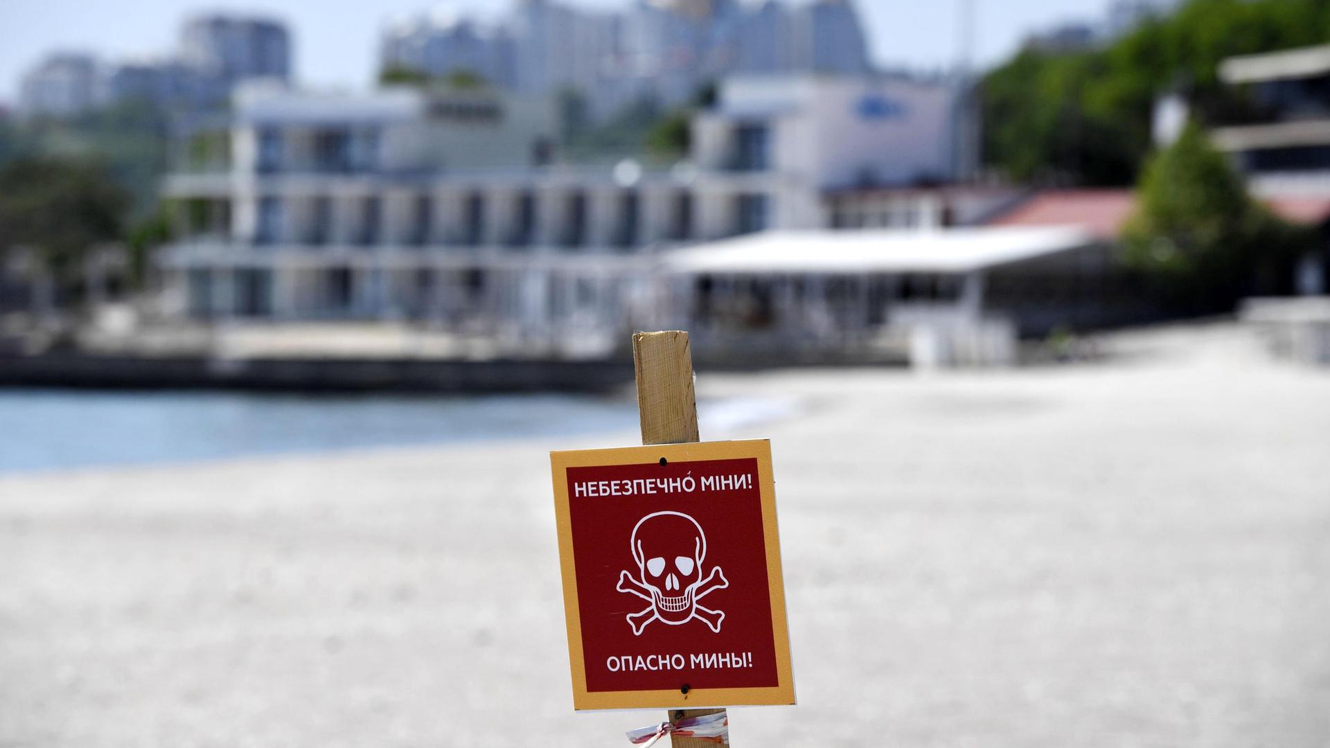 Ein Schild an einem Strand in Odessa in der südlichen Ukraine warnt vor Landminen. Im Hintergrund sind Gebäude zu sehen.