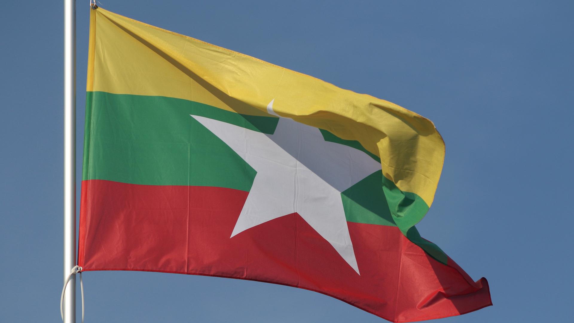 Die Nationalfahne von Myanmar flattert im Wind vor einem blauen Himmel. 