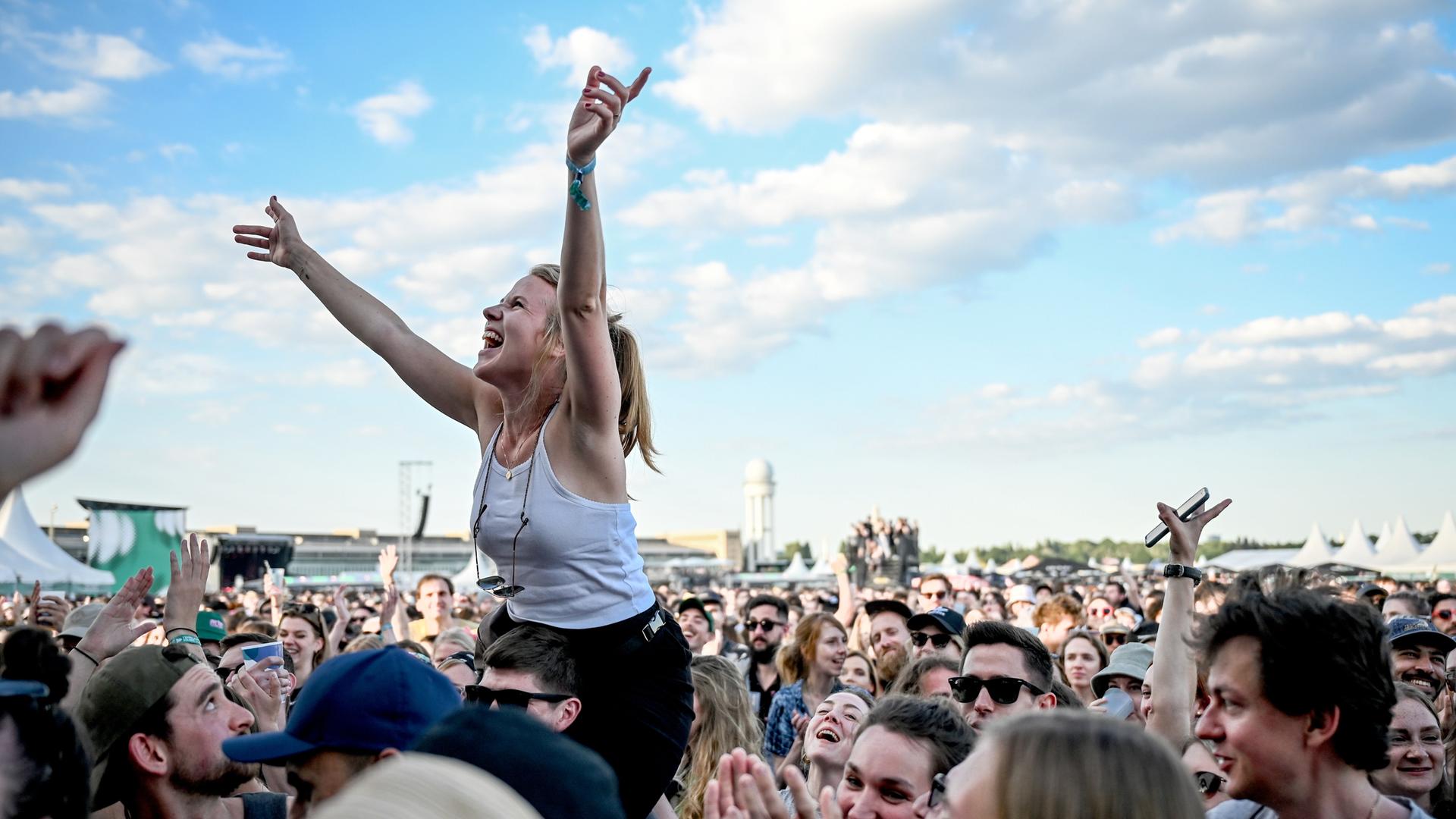 Das Publikum feiert beim Tempelhof-Sounds Festival auf dem Gelände des ehemaligen Flughafen Berlin Tempelhof. Eine junge Frau ist auf den Schultern eines anderen Besuchers und freut sich.