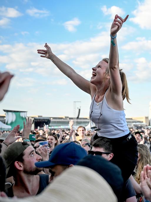 Das Publikum feiert beim Tempelhof-Sounds Festival auf dem Gelände des ehemaligen Flughafen Berlin Tempelhof. Eine junge Frau ist auf den Schultern eines anderen Besuchers und freut sich.