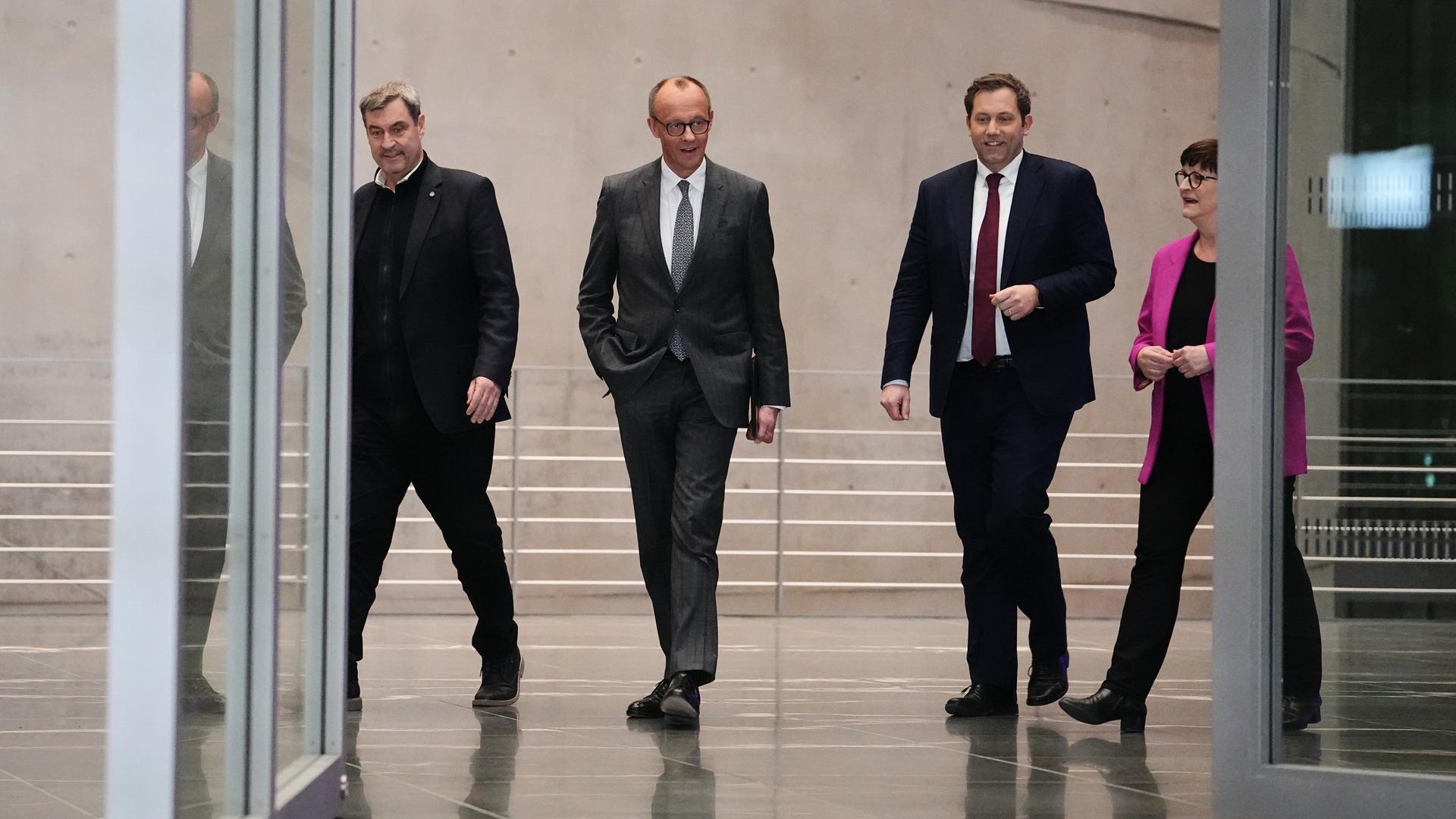 Markus Söder, Friedrich Merz, Lars Klingbeil und Saskia Esken laufen nebeneinander durch eine Tür zu einer Pressekonferenz.