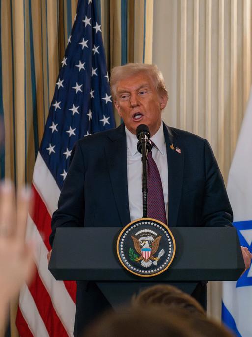 Donald Trump am Rednerpult. Im Vordergrund sieht man verschwommene erhobene Hände von Journalisten. Donald Trump am Rednerpult. Im Vordergrund sieht man verschwommene erhobene Hände von Journalisten.