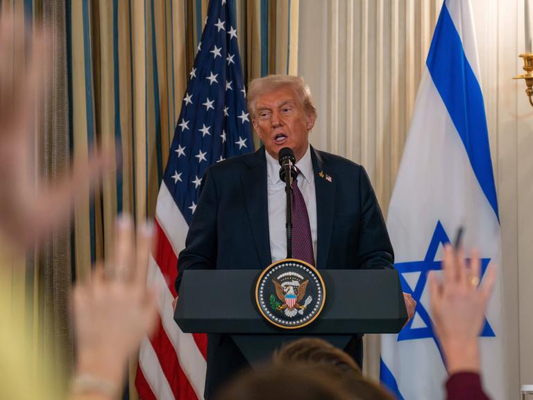 Donald Trump am Rednerpult. Im Vordergrund sieht man verschwommene erhobene Hände von Journalisten. Donald Trump am Rednerpult. Im Vordergrund sieht man verschwommene erhobene Hände von Journalisten.