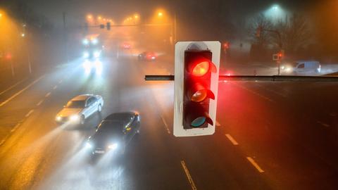 Autos passieren am frühen Morgen bei dichtem Nebel eine Kreuzung mit einer Ampel, die rot ist.
