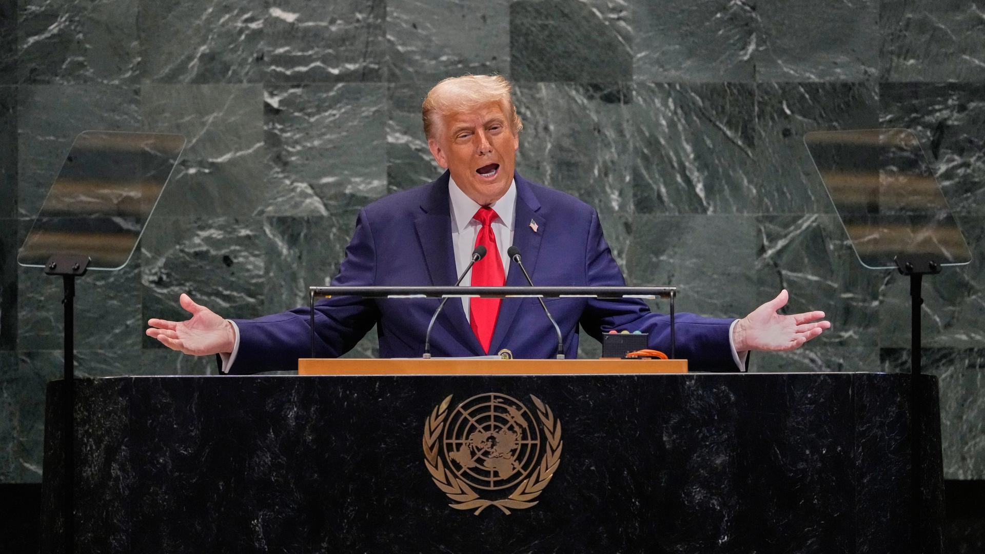 Donald Trump spricht mit ausgebreiteten Armen an einem Rednerpult mit dem Wappen der Vereinten Nationen.