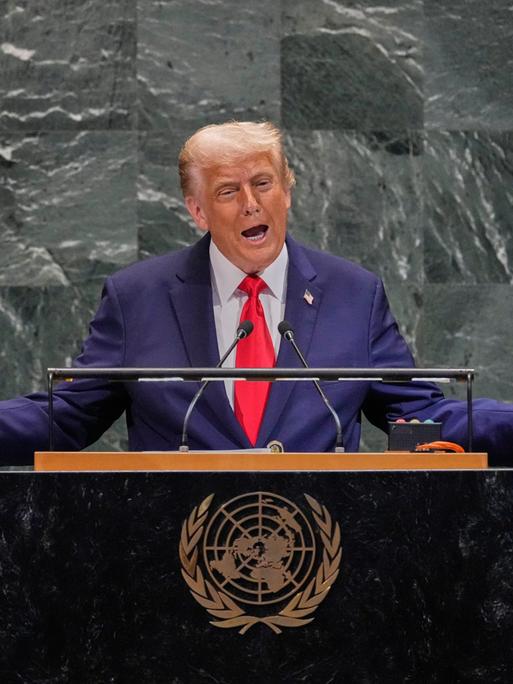 Donald Trump spricht mit ausgebreiteten Armen an einem Rednerpult mit dem Wappen der Vereinten Nationen.