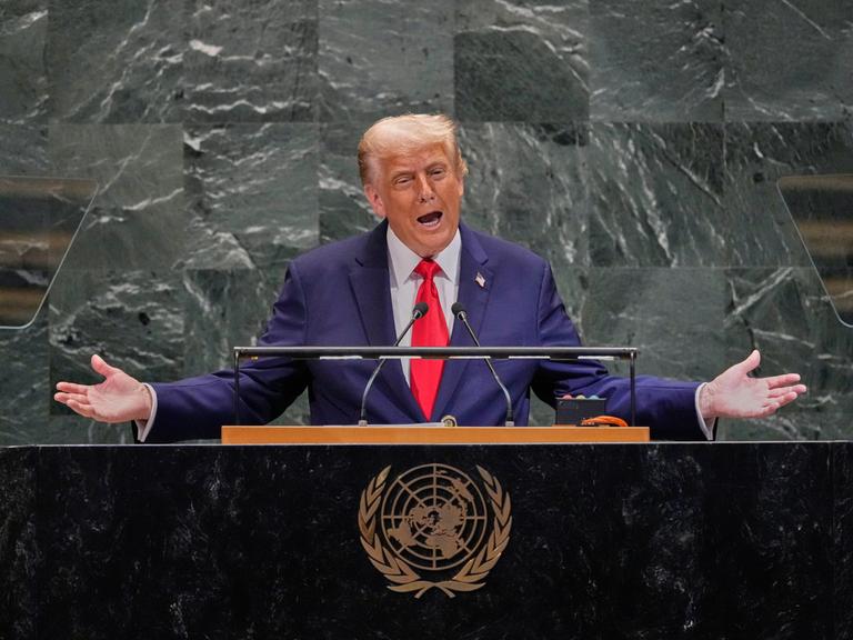 Donald Trump spricht mit ausgebreiteten Armen an einem Rednerpult mit dem Wappen der Vereinten Nationen.