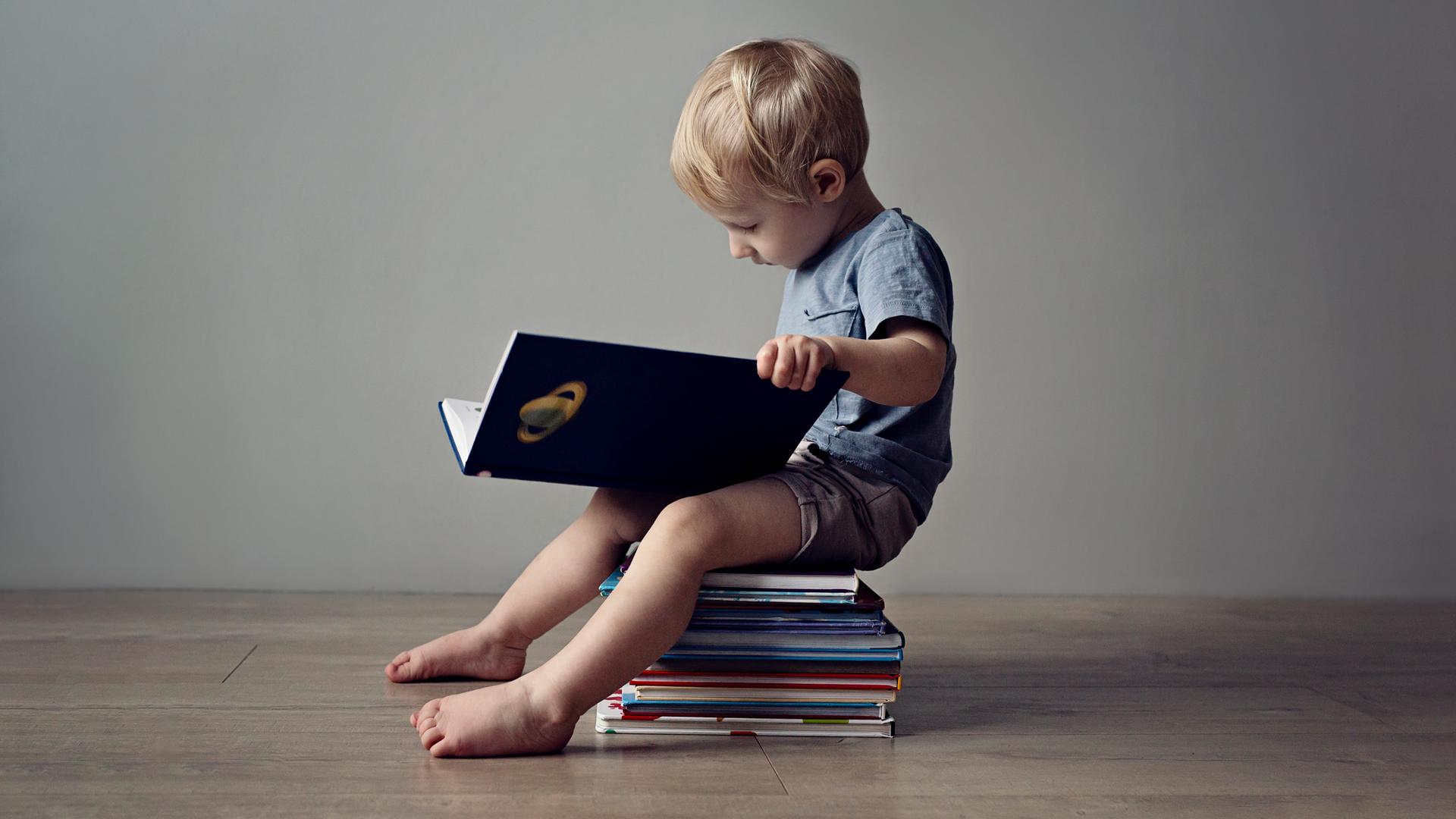Ein kleiner Junge mit BUch in der Hansd sitzt auf einem Bücherstapel und liest Ein kleiner Junge mit BUch in der Hansd sitzt auf einem Bücherstapel und liest