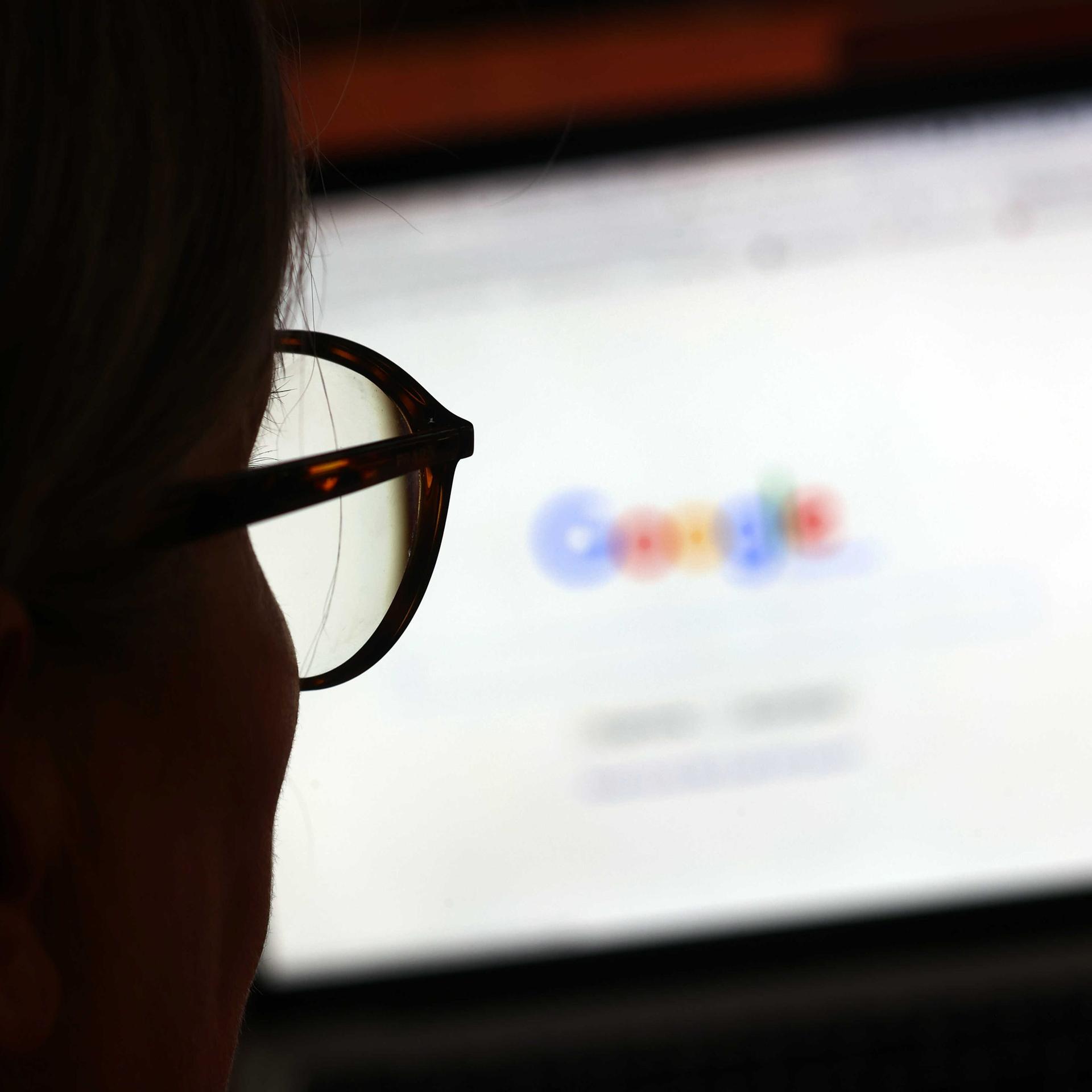 Die Seite der Suchmaschine von Google ist hinter einer Frau mit Brille zu sehen.