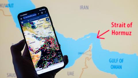 Farbige Punkte auf einem Display zeigen, wie viele Schiffe in der von Iran blockierten Straße von Hormus festliegen. Im Hintergrund eine Landkarte, die den Iran und seine Nachbarstaaten zeigt.