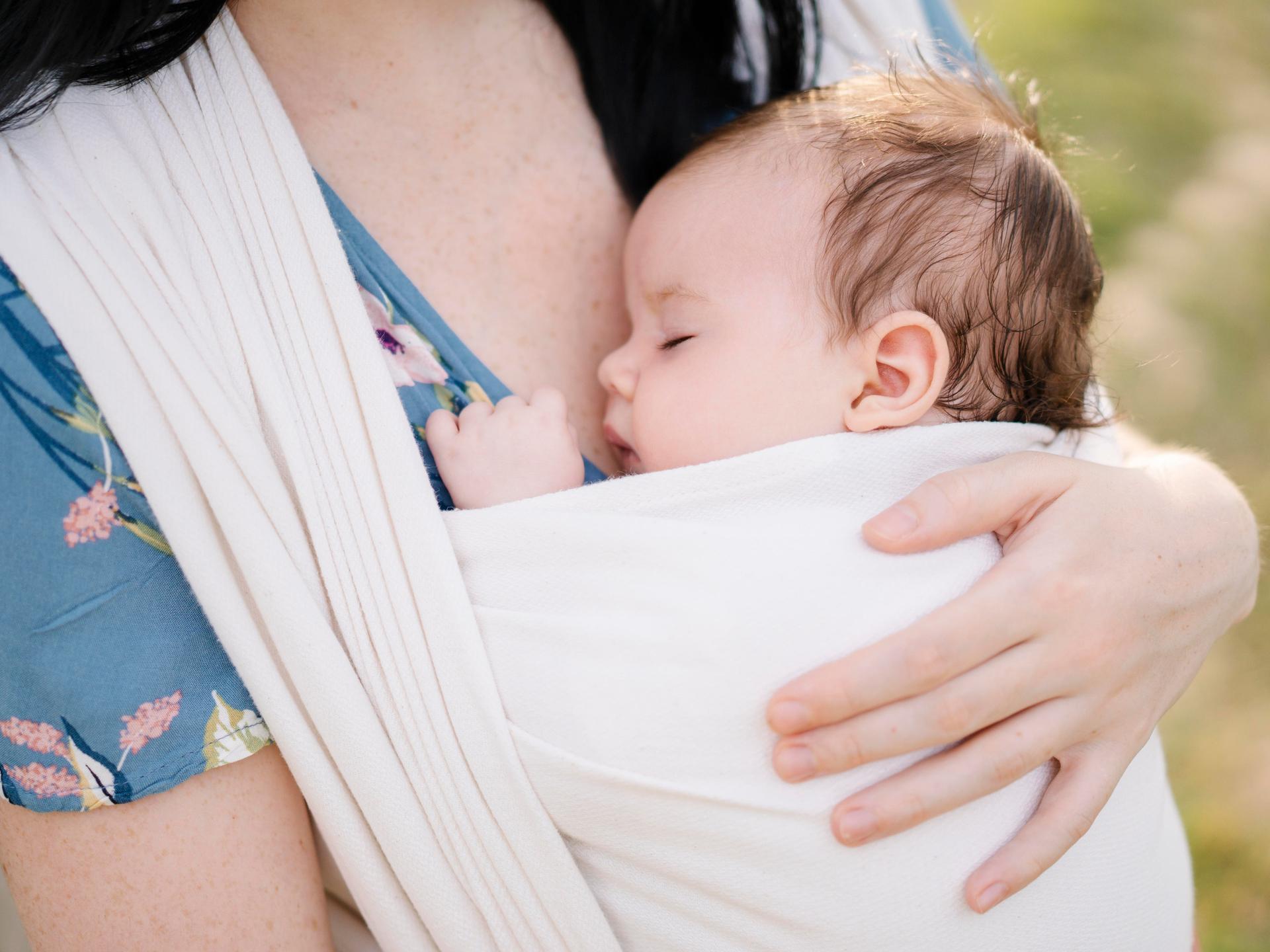 Eine Mutter trägt ein schlafendes Baby, das in einem Tuch gewickelt ist. 