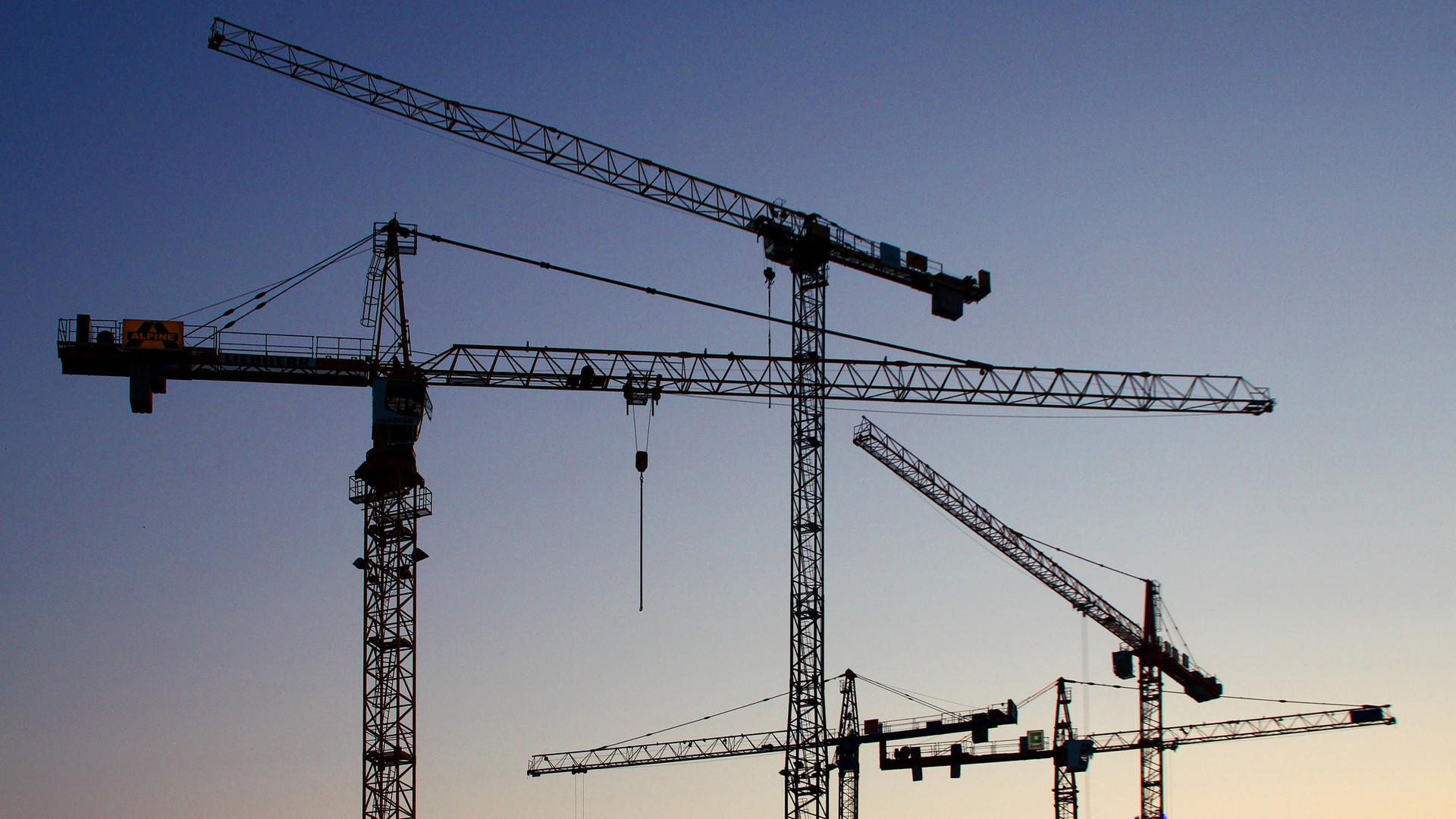 Baukräne stehen in der Dämmerung.