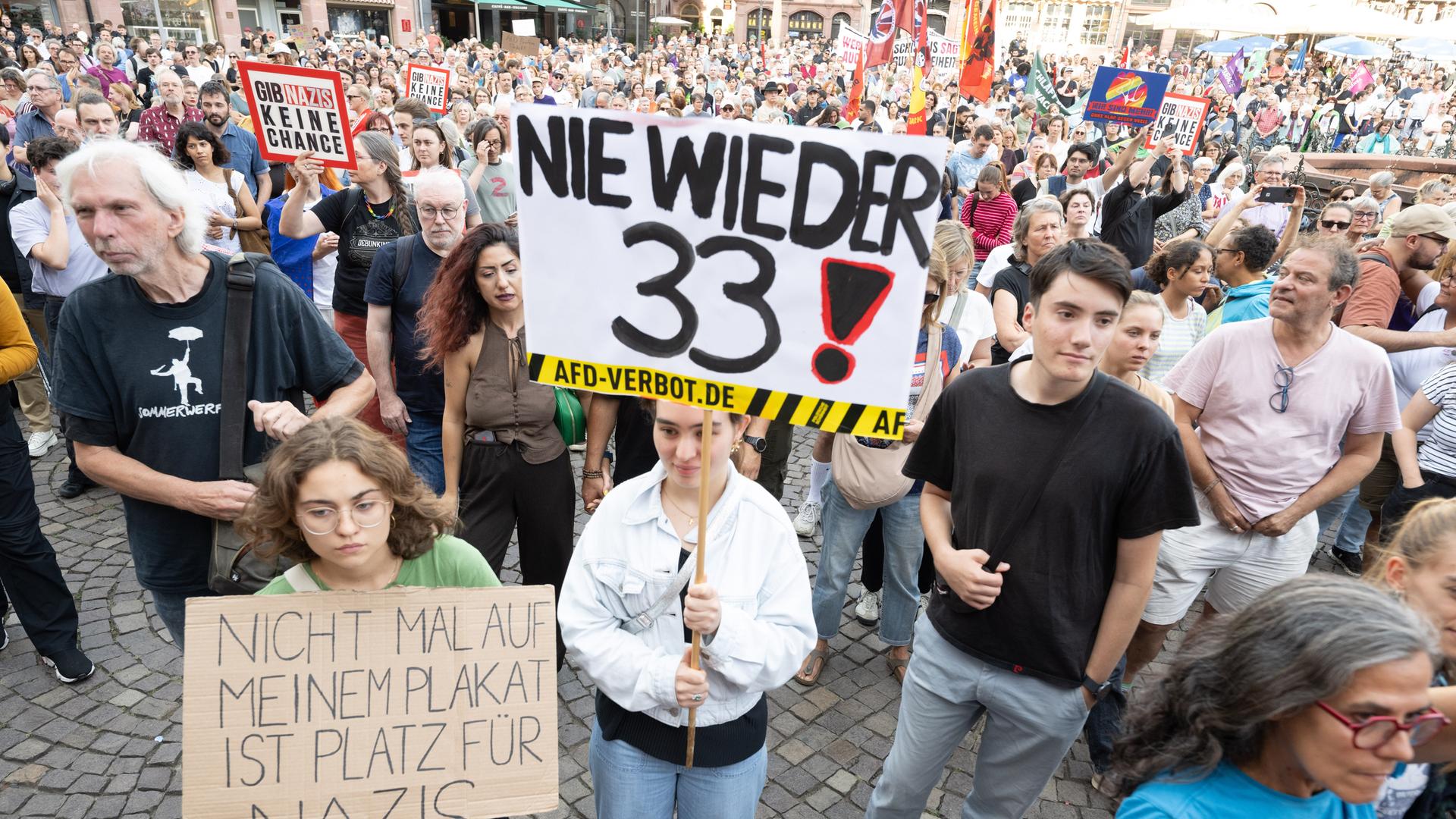 Viele Menschen stehen auf einem Platz, einige halten Plakate und Banner hoch. Auf einem Plakat weit vorne steht "Nie wieder 33". Viele Menschen stehen auf einem Platz, einige halten Plakate und Banner hoch. Auf einem Plakat weit vorne steht "Nie wieder 33".