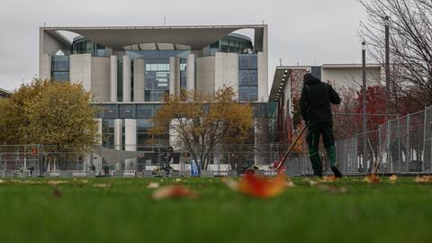 Ein Mensch recht Laub vor dem Kanzleramt. Am Mittwochabend entließ der Bundeskanzler den Finanzminister und kündige Neuwahlen für das kommende Frühjahr an.