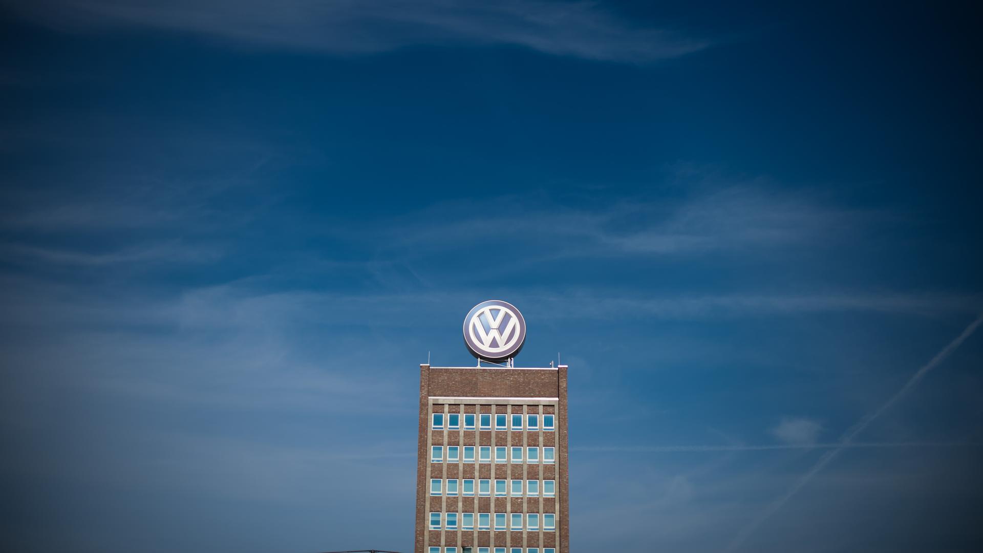 Blauer Himmel über dem Hochhaus, dessen obere Hälfte mit dem VW-Zeichen auf der Spitze aus der Ferne fotografiert ist. 