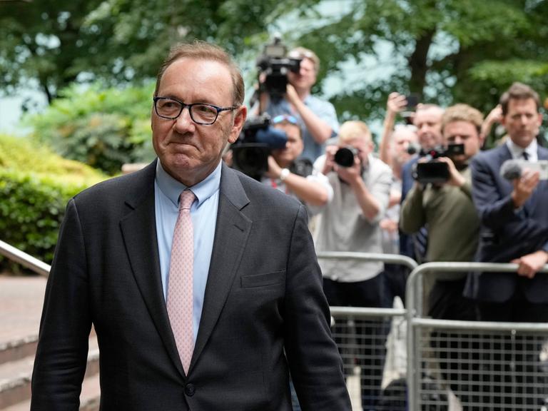 Kevin Spacey verlässt den Southwark Crown Court und lächelt. Im Hintergrund stehen viele Fotografen.