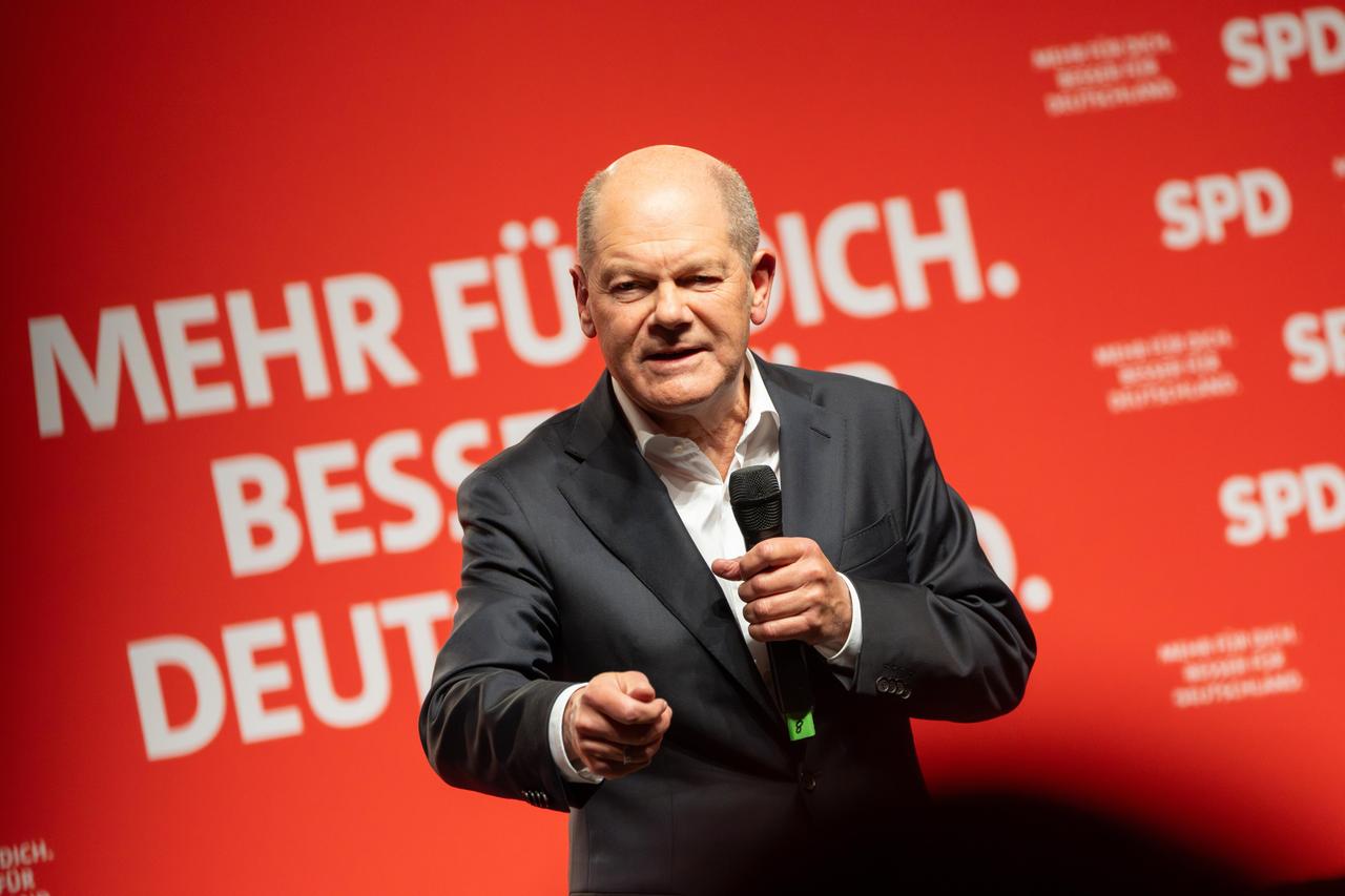 Olaf Scholt steht vor einer roten Wand mit dem SPD-Logo und spricht.