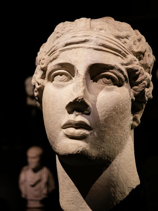 Die Plastik eines antiken Frauenkopfes soll Sappho darstellen. Sie zeigt in ihrem Haar ein Band, während ihr Blick nach oben gerichtet ist.