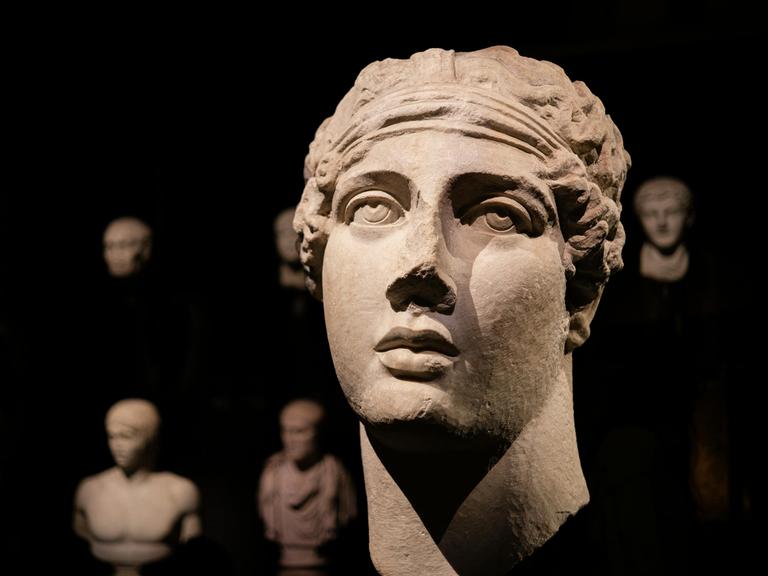 Die Plastik eines antiken Frauenkopfes soll Sappho darstellen. Sie zeigt in ihrem Haar ein Band, während ihr Blick nach oben gerichtet ist.