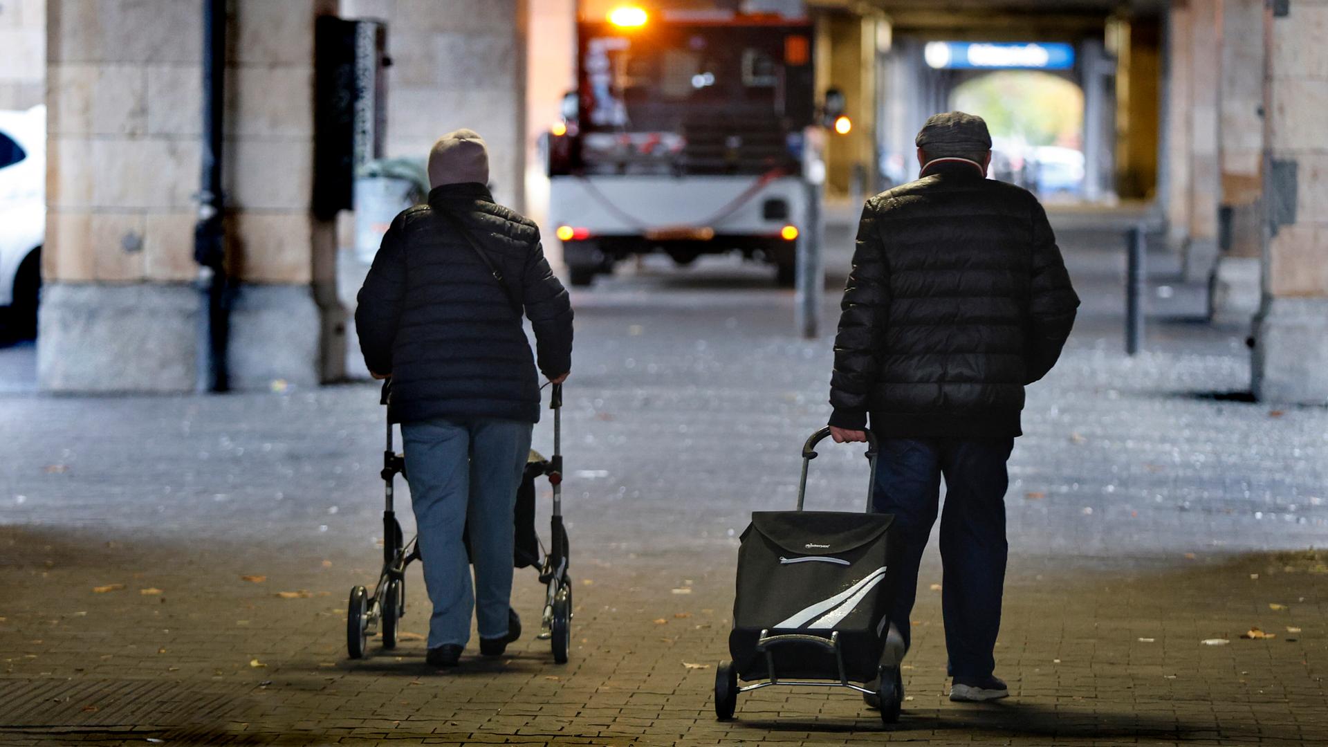 Rentnerpaar mit Rolator und Einkaufswagen in einer Unterführung im Halbdunkeln Rentnerpaar mit Rolator und Einkaufswagen in einer Unterführung im Halbdunkeln