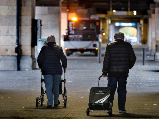 Rentnerpaar mit Rolator und Einkaufswagen in einer Unterführung im Halbdunkeln Rentnerpaar mit Rolator und Einkaufswagen in einer Unterführung im Halbdunkeln