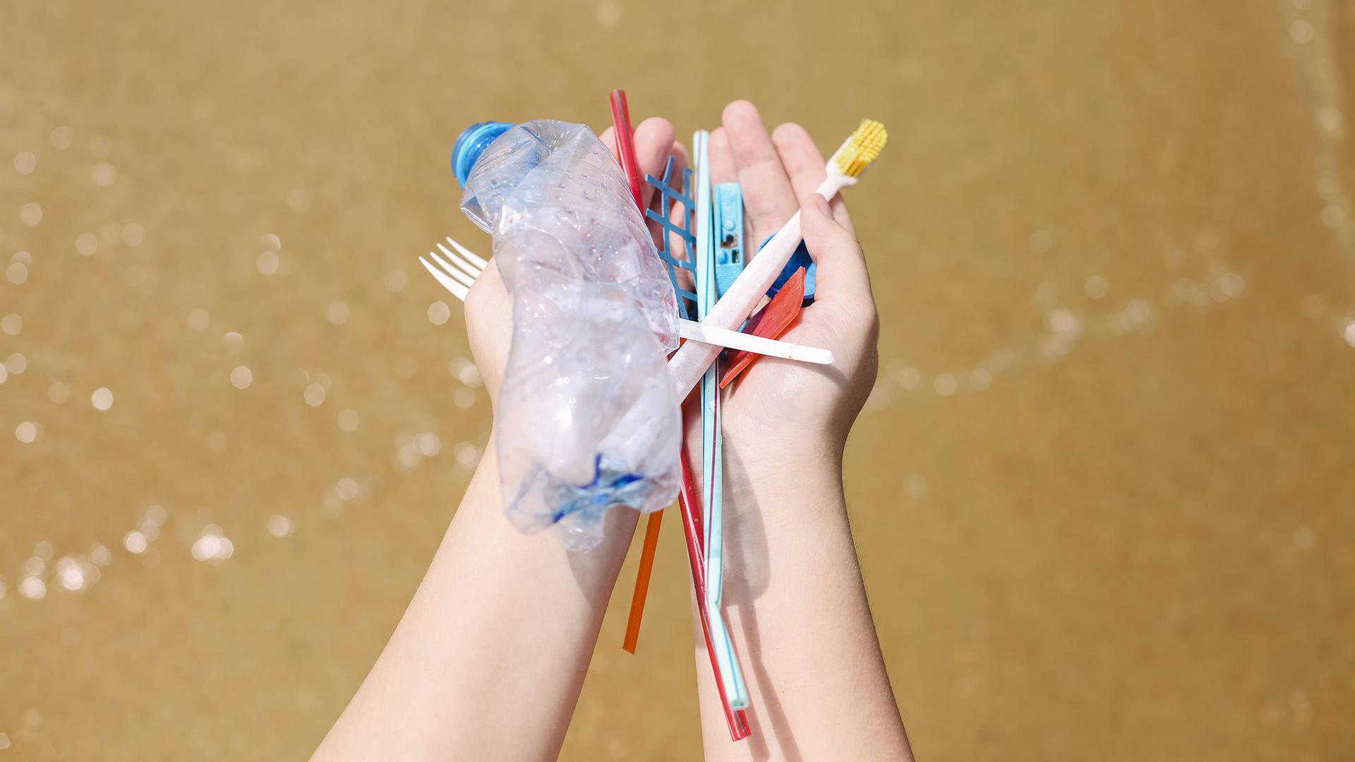 Hände halten Plastikmüll am Strand, alte Zahnbürsten, Plastikflaschen und Plastikstücke.