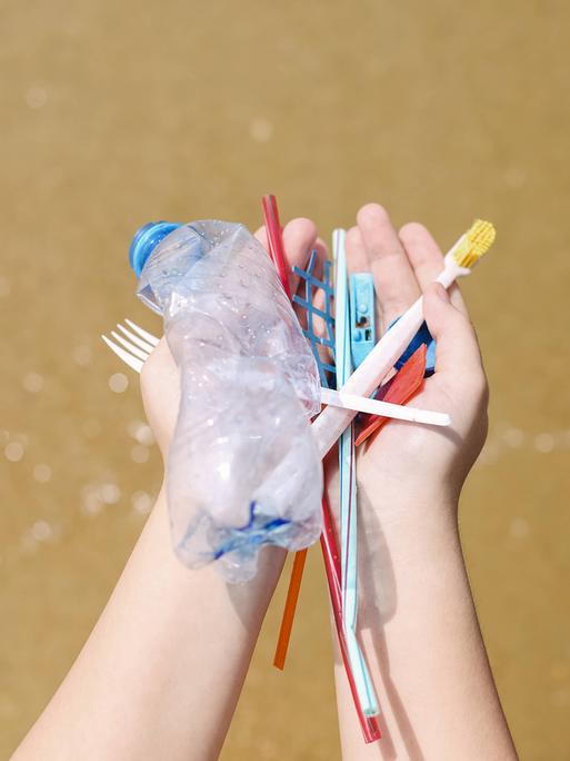 Hände halten Plastikmüll am Strand, alte Zahnbürsten, Plastikflaschen und Plastikstücke.