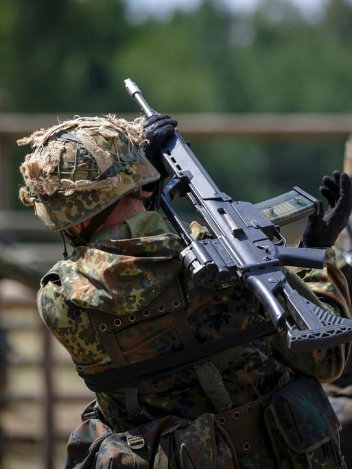 Drei Rekruten marschieren auf einem Gelände, sie haben Gewehre geschultert. Alle drei tragen Tarnanzüge und sind von hinten zu sehen.