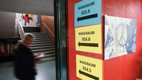 Ein Wähler geht über einen Schulkorridor; im Vordergrund weisen bunte Schilder den Weg zu mehreren Wahlräumen.