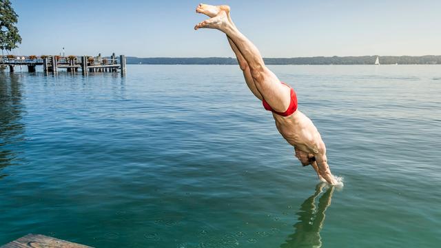 Ein Mann mit Bade-Hose springt kopf-über in einen See.
