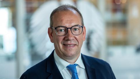 Henning Otte (CDU), aufgenommen nach seiner Wahl als neuer Wehrbeauftragter des Bundestags. Er lächelt verhalten. Im Hintergrund ist unscharf der Bundesadler auf einer Glasscheibe zu erkennen. 