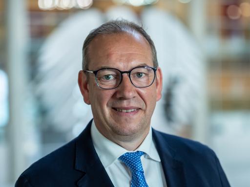 Henning Otte (CDU), aufgenommen nach seiner Wahl als neuer Wehrbeauftragter des Bundestags. Er lächelt verhalten. Im Hintergrund ist unscharf der Bundesadler auf einer Glasscheibe zu erkennen. 