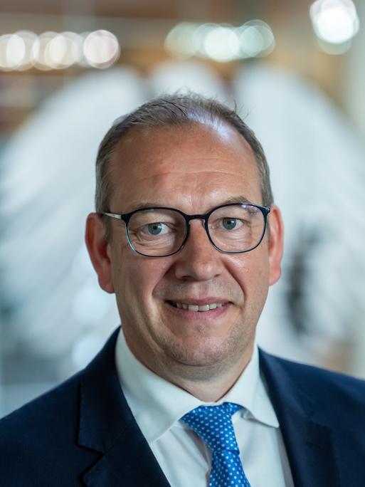 Henning Otte (CDU), aufgenommen nach seiner Wahl als neuer Wehrbeauftragter des Bundestags. Er lächelt verhalten. Im Hintergrund ist unscharf der Bundesadler auf einer Glasscheibe zu erkennen. 