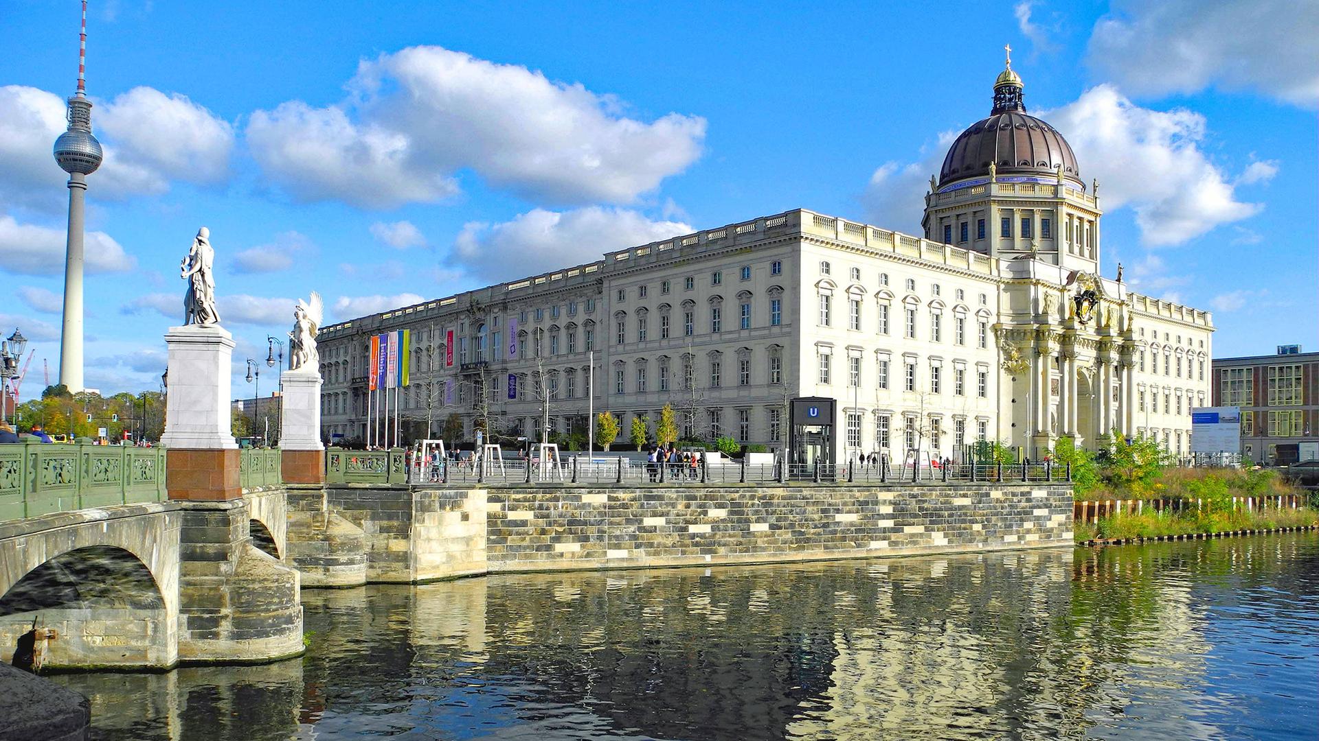 In der Mitte das Humboldt Forum in Berlin. Davor Wasser. Im Hintergrund ist links auch der Fernsehturm am Alexanderplatz zu erkennen.