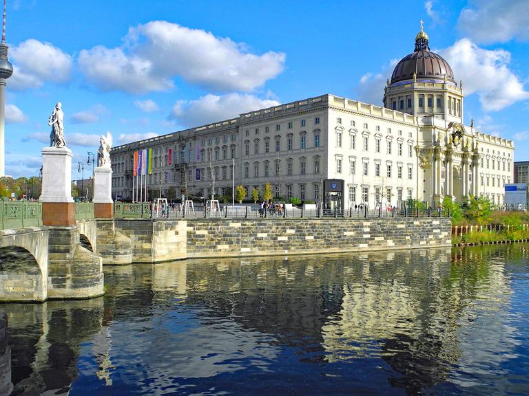 In der Mitte das Humboldt Forum in Berlin. Davor Wasser. Im Hintergrund ist links auch der Fernsehturm am Alexanderplatz zu erkennen.