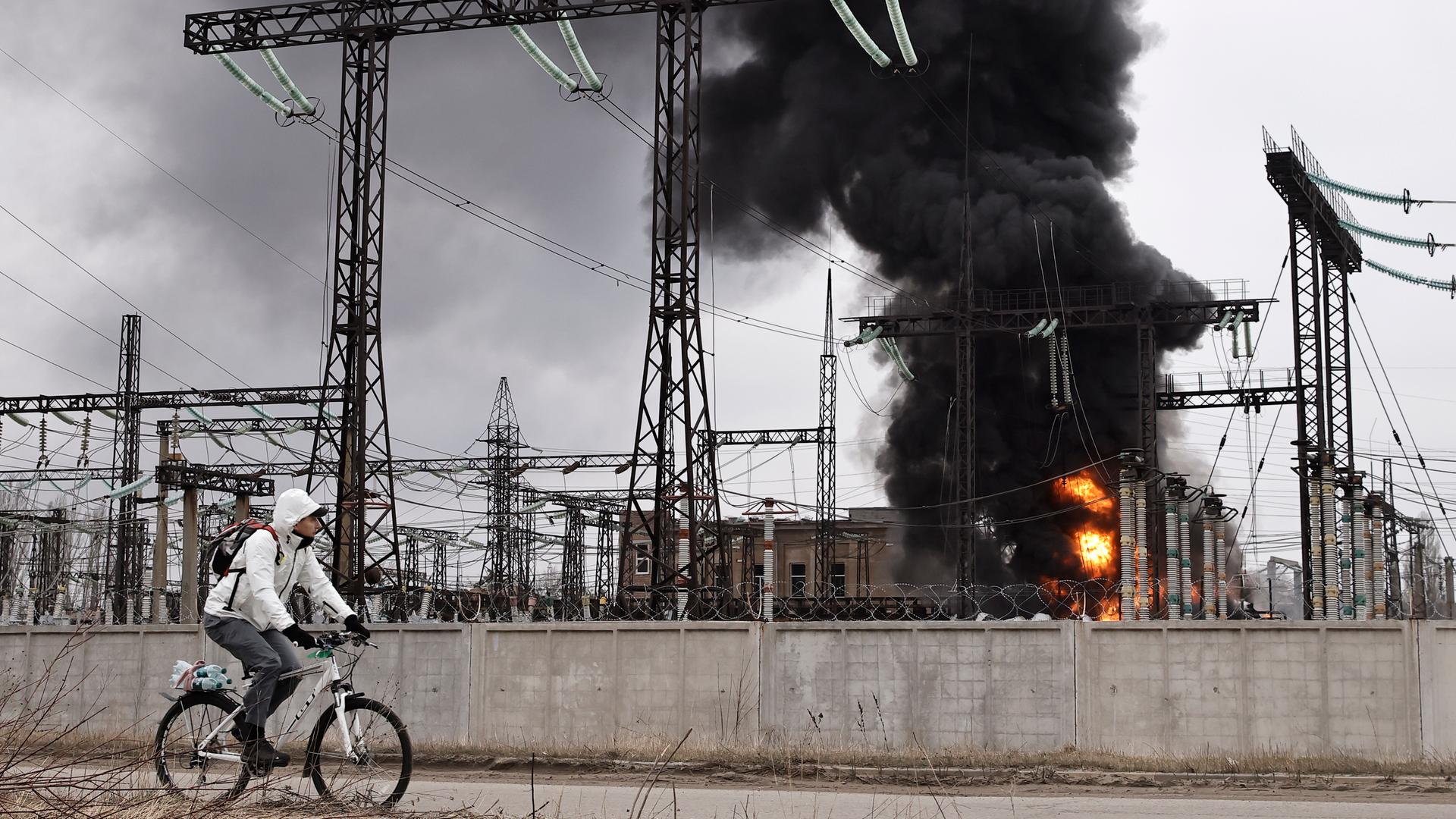 Ukraine, Charkiw: Ein Mann radelt nach einem russischen Angriff an einem Elektrizitätswerk vorbei. Rauch steigt auf. 