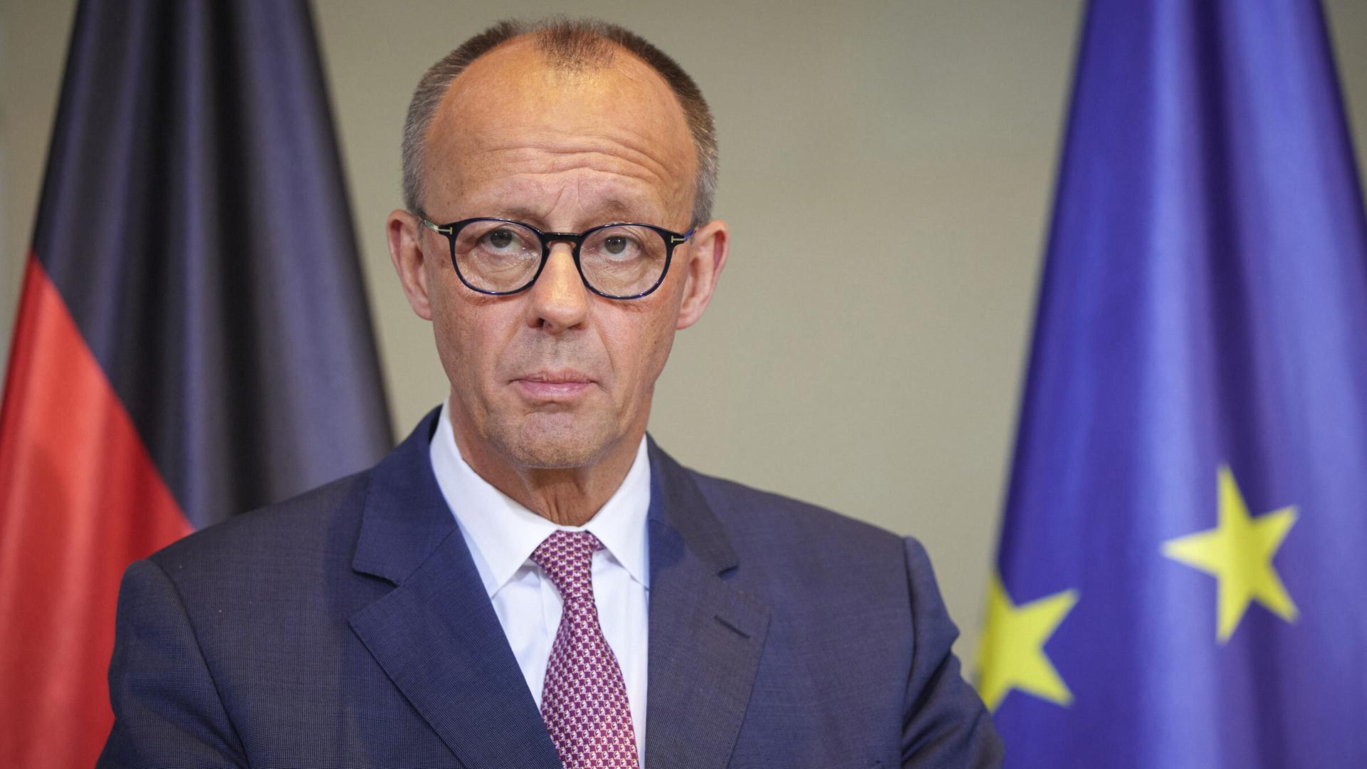 Bundeskanzler Friedrich Merz steht an einem Rednerpult, im Hintergrund sieht man im Anschnitt eine Deutschland- und eine Europa-Flagge.