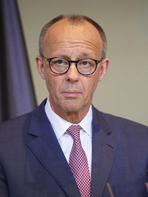 Bundeskanzler Friedrich Merz steht an einem Rednerpult, im Hintergrund sieht man im Anschnitt eine Deutschland- und eine Europa-Flagge.